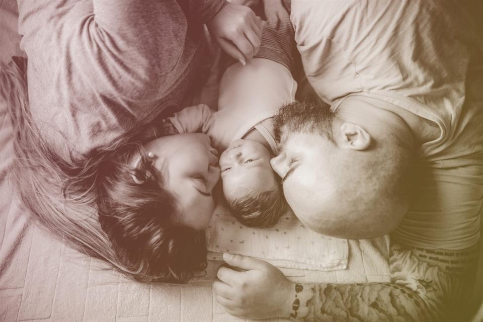 couple laying down with baby in between giving kiss on cheek