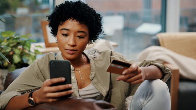 Shot of a young woman holding her credit card while using her cellphone at home.