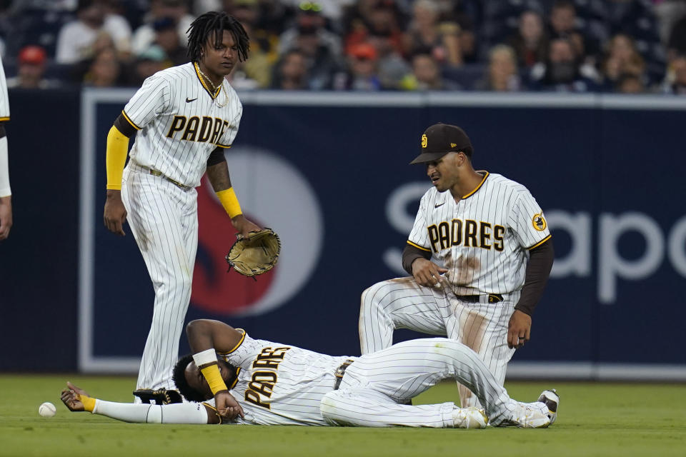 San Diego Padres left fielder Jurickson Profar, bottom, reacts after colliding with shortstop C.J. Abrams, left, as center fielder Trent Grisham, right, looks on during the fifth inning of a baseball game against the San Francisco Giants, Thursday, July 7, 2022, in San Diego. Profar and Abrams collided as Abrams made a catch for an out against Giants' Tommy La Stella. (AP Photo/Gregory Bull)