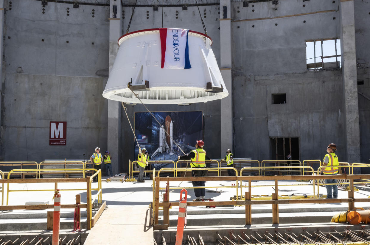  workers in yellow vests guide part of a white solid rocket booster to the floor 