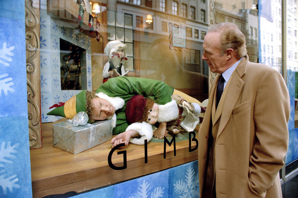 a large elf sitting in a store display window as a man looks curiously at him