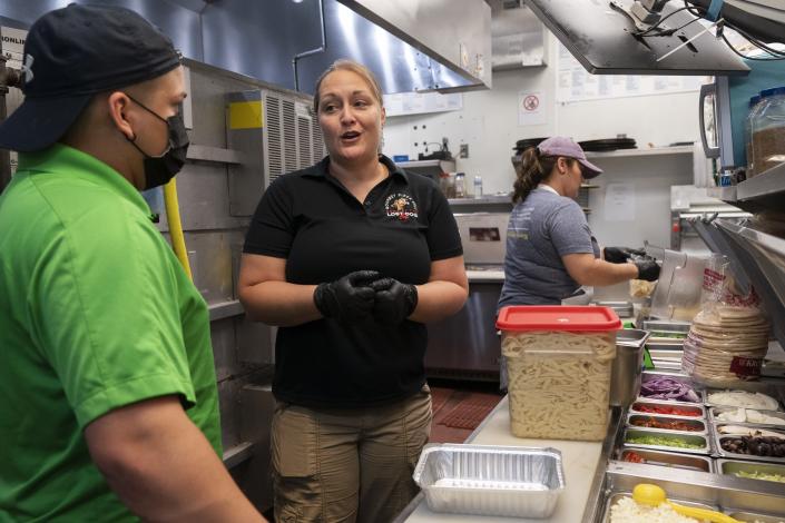 Sarah White, center, area manager of Lost Dog Cafe, trains manager Alex Aleman, left, in a new pasta preparation technique, as they work at the cafe in Fairfax, Va., on Friday, Aug. 27, 2021. Lost Dog is one of a growing number of companies that, in a desperation for hired hands, is loosening restrictions on everything from age to level of experience. (AP Photo/Jacquelyn Martin)