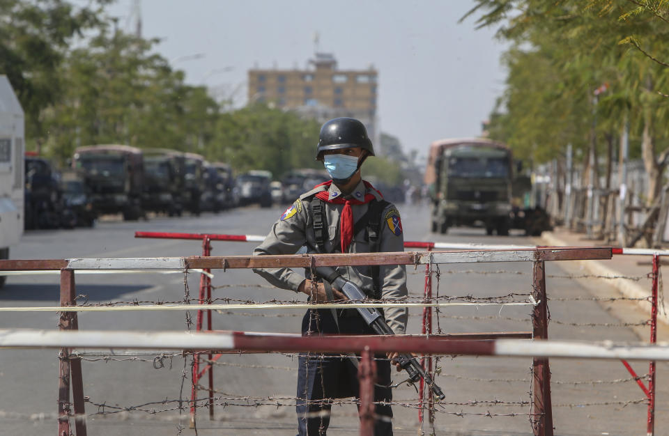 An armed police officer stands guard along a cordoned-off road with police vehicles and water cannons, the site of clashes a day earlier in Mandalay, Myanmar on Wednesday, Feb. 10, 2021. Protesters continued to gather Wednesday morning in Mandalay breaching Myanmar's new military rulers' decrees that effectively banned peaceful public protests in the country's two biggest cities. (AP Photo)