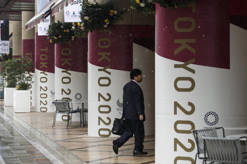 A man walks into a building decorated with Tokyo 2020 banners Tuesday, July 23, 2019, in Tokyo. To mark the year-to-go mark, the gold, silver and bronze Olympic medals are to be unveiled Wednesday as part of daylong ceremonies around the Japanese capital. Tokyo's 1964 Olympics showcased bullet trains, futuristic designs and a new expressway, underlining Japan's recovery following World War II. Those games were the first seen worldwide by early satellites, sending the Olympics into a new era. (AP Photo/Jae C. Hong)