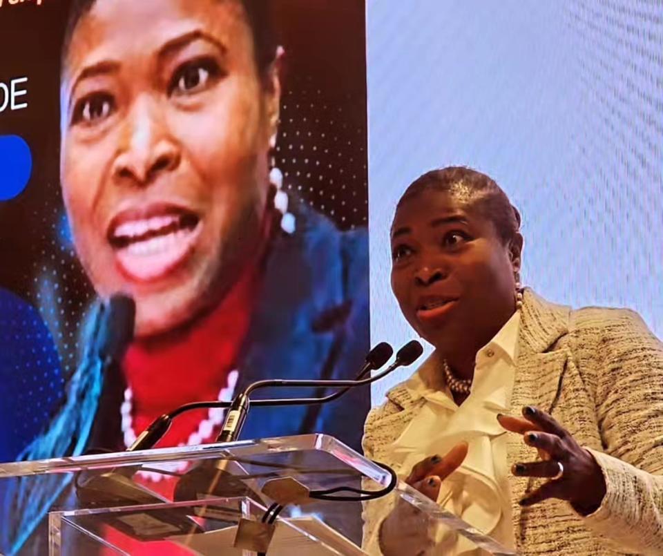 Woman speaking at podium with her image projected on screen behind her