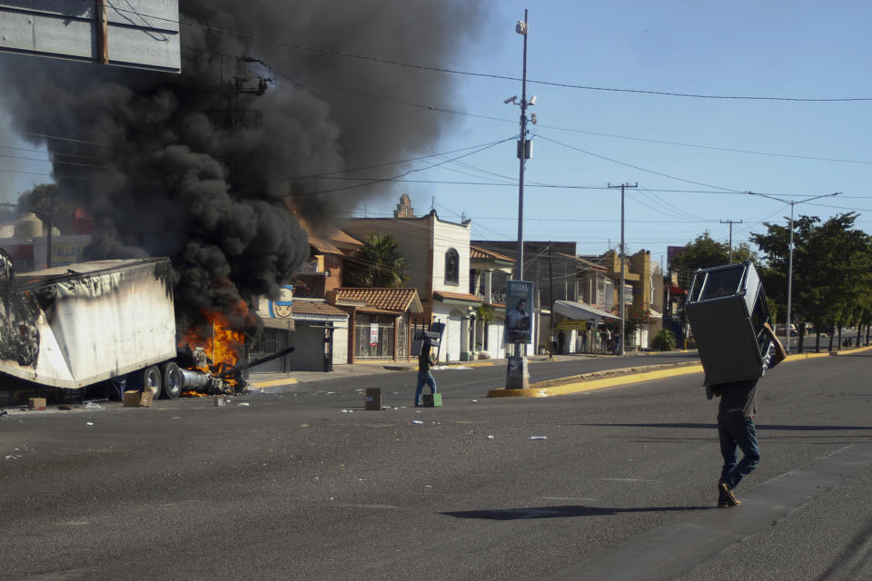 Men carry furniture after looting a store, as a truck burns on a street in Culiacan, Sinaloa state, Thursday, Jan. 5, 2023. Mexican security forces captured Ovidio Guzmán, an alleged drug trafficker wanted by the United States and one of the sons of former Sinaloa cartel boss Joaquín “El Chapo” Guzmán, in a pre-dawn operation Thursday that set off gunfights and roadblocks across the western state’s capital. (AP Photo/Martin Urista)