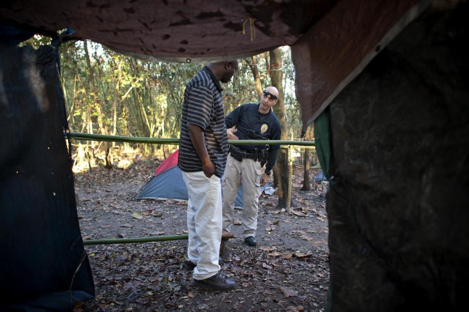 In this Monday, Dec. 9, 2013 photo, Homeless Liaison Officer Tom Gentner, right, tries to make eye contact with a homeless man known as "K.B." who started a fight with residents in an area called the Bamboo Forest in Savannah, Ga. Gentner documents, monitors and mediates all 20 camps in the area, keeping the peace and monitoring the activities of the diverse population. (AP Photo/Stephen B. Morton)