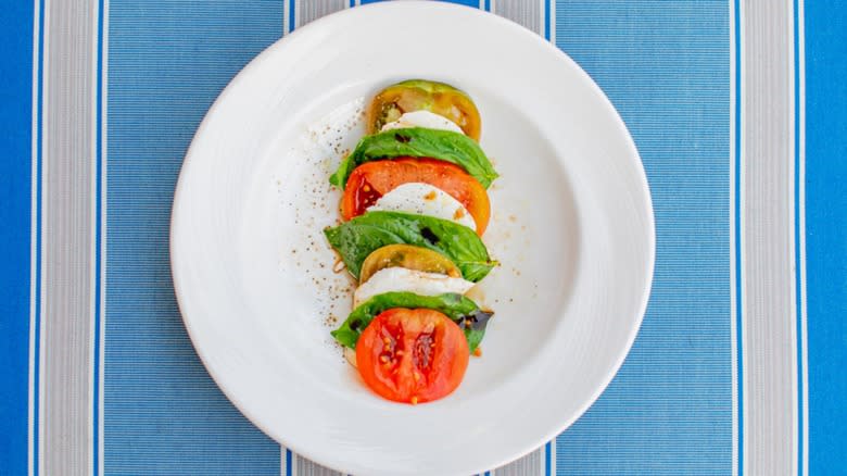 Caprese salad on white plante with striped blue tablecloth