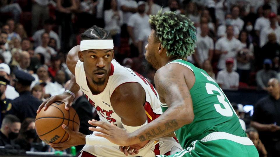 jimmy butler, wearing a white miami heat jersey, is covered by marcus smart, wearing a green boston celtics jersey, during a basketball game