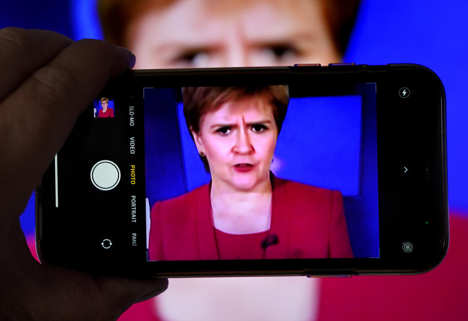 <p>A person uses their phone to film a televised broadcast of First Minister Nicola Sturgeon speaking to MSPS during a virtual sitting of the Scottish Parliament. Picture date: Tuesday August 3, 2021.</p>
