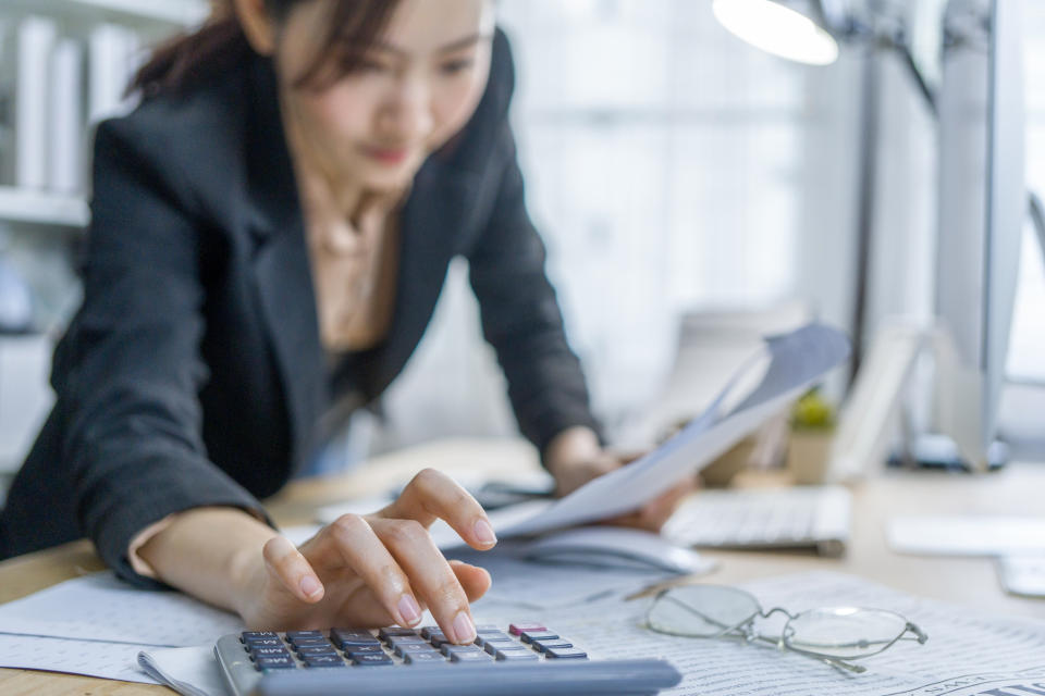 A person using a calculator while looking at documents on a cluttered desk, indicating financial calculations