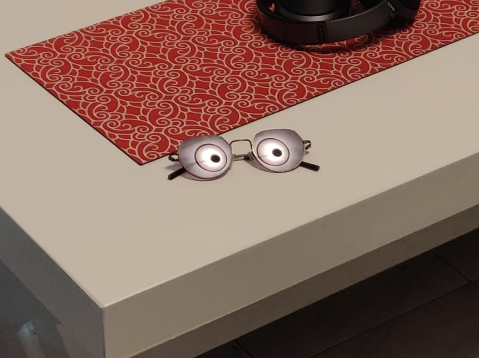 A pair of eyeglasses and headphones are on a white table with a red patterned runner