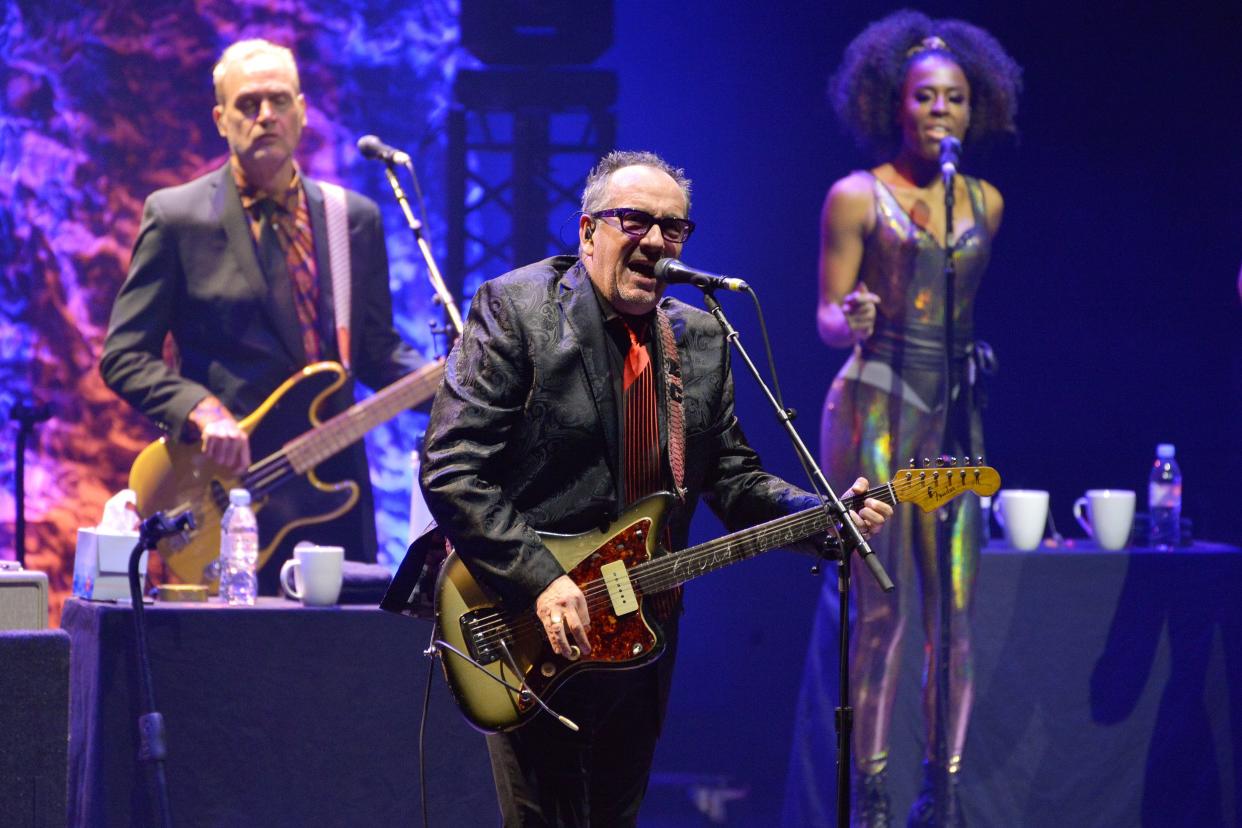 Elvis Costello performs live on stage with The Imposters at the Hammersmith Apollo on March 13, 2020 in London, purple and blue lighting