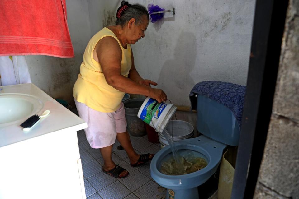 A woman pours water from a bucket into a toilet