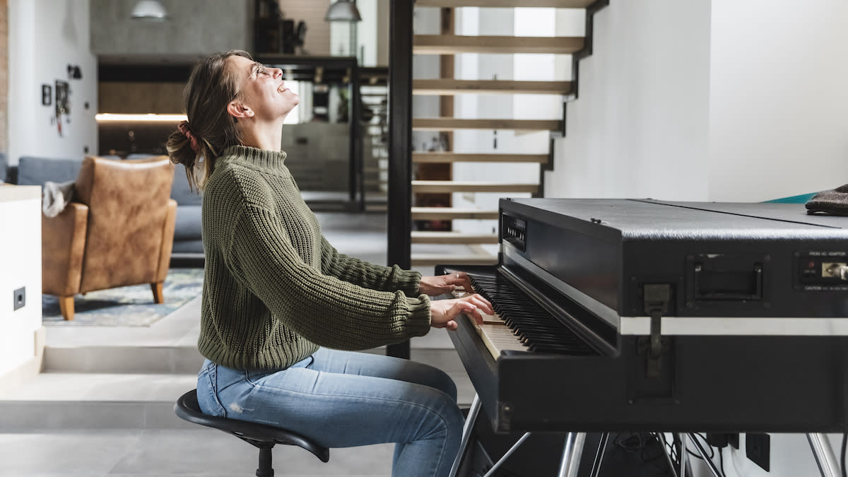  Smiling woman in green jumper sits at a piano. 