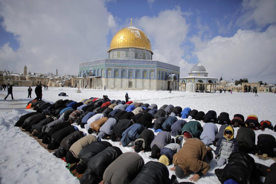 Palestinian men pray in front of the snow-covered Dome of the Rock, in Jerusalem's Old City