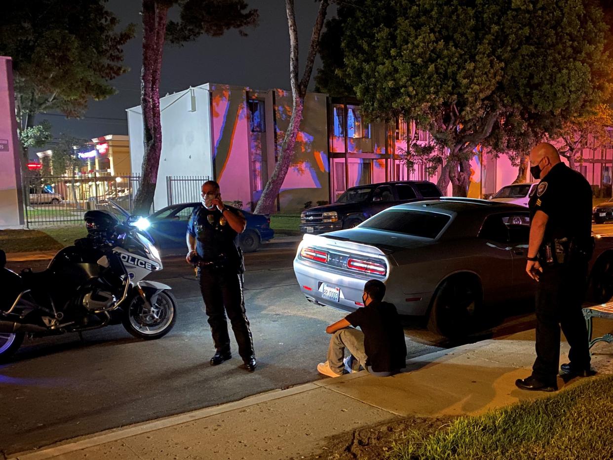 A driver sits on the sidewalk after being pulled over during street-racing enforcement operation Thursday, Aug. 20, 2020, in Oxnard, Calif.