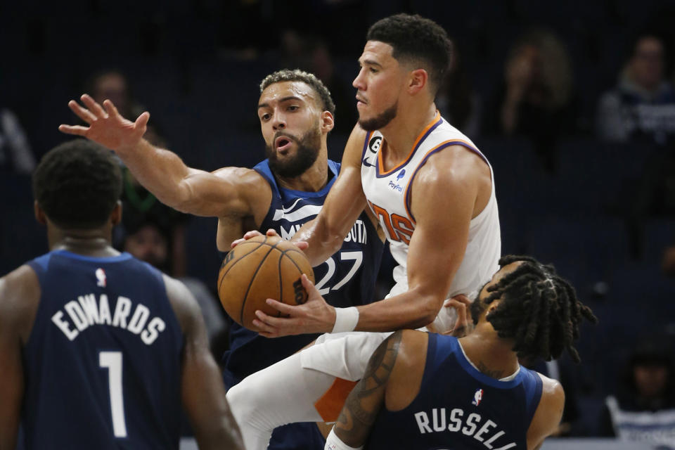 Phoenix Suns guard Devin Booker, middle, goes between Minnesota Timberwolves center Rudy Gobert (27) and guard D'Angelo Russell during the fourth quarter of an NBA basketball game Wednesday, Nov. 9, 2022, in Minneapolis. The Suns won 129-117. (AP Photo/Bruce Kluckhohn)