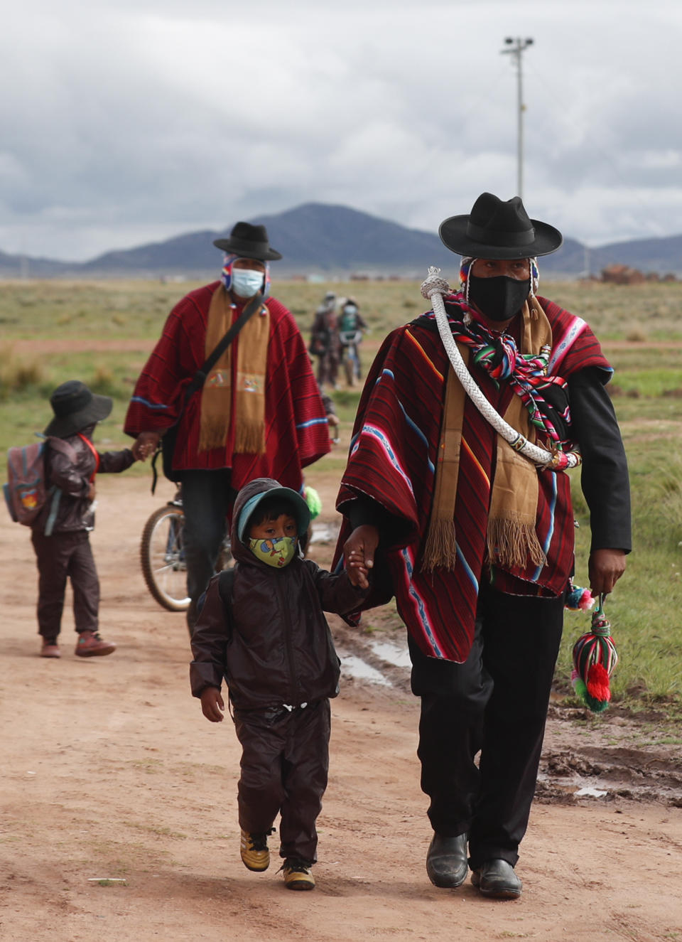 Aymara Indigenous fathers walk their children wearing new, protective uniforms amid the COVID-19 pandemic to Jancohaqui Tana school during their first week back to class amid the pandemic near Jesus de Machaca, Bolivia, early Thursday, Feb. 4, 2021. (AP Photo/Juan Karita)