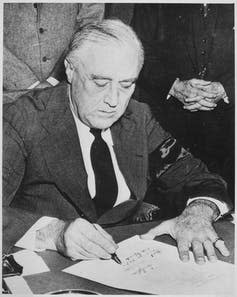 A man in a coat and tie signs a document.