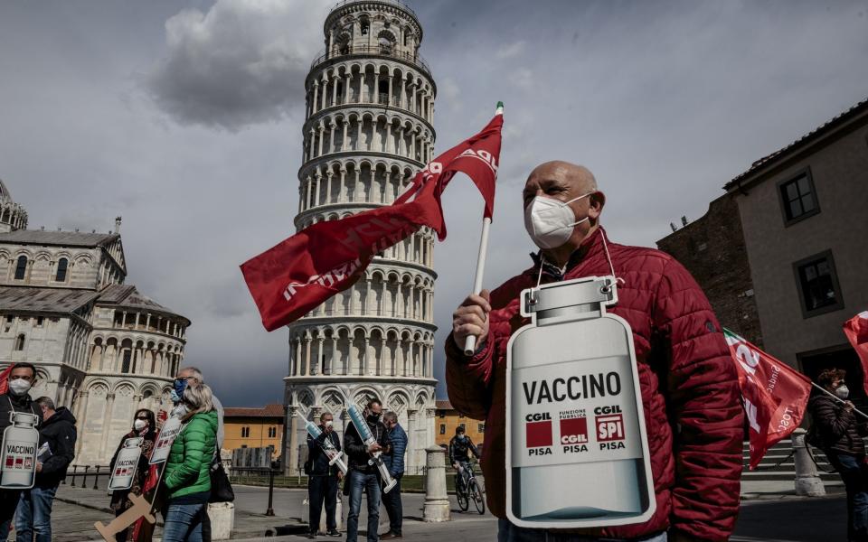 A retired man standing with a cardboard sign of the shape of a covid vaccine in front of the leaning tower in Pisa, Italy - Enrico Mattia Del Punta/NurPhoto