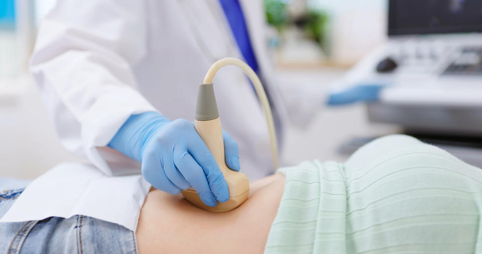 A healthcare professional performs an ultrasound on a patient's abdomen, using a handheld device while wearing blue gloves