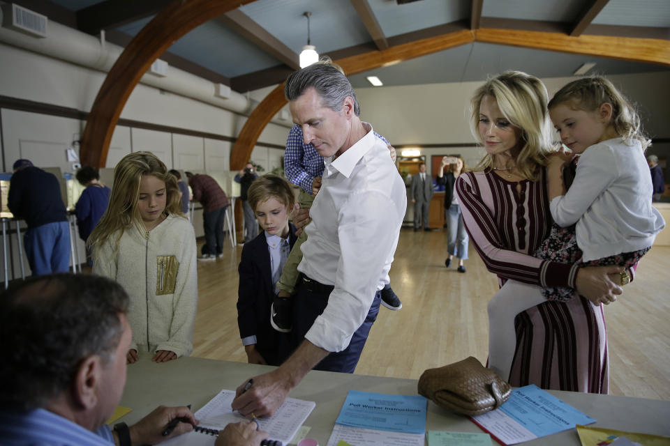 FILE -- In this Nov. 6, 2018 file photo California gubernatorial Democratic candidate Gavin Newsom signs in to vote as family looks on in Larkspur, Calif. From left is his daughter Montana, 9, son Hunter, 7, his wife, Jennifer Siebel Newsom, and daughter Brooklynn, 7. Siebel Newsom has shunned the traditional title of "first lady" and is focusing on women's issues including equal pay and expanding family leave. (AP Photo/Eric Risberg, File)