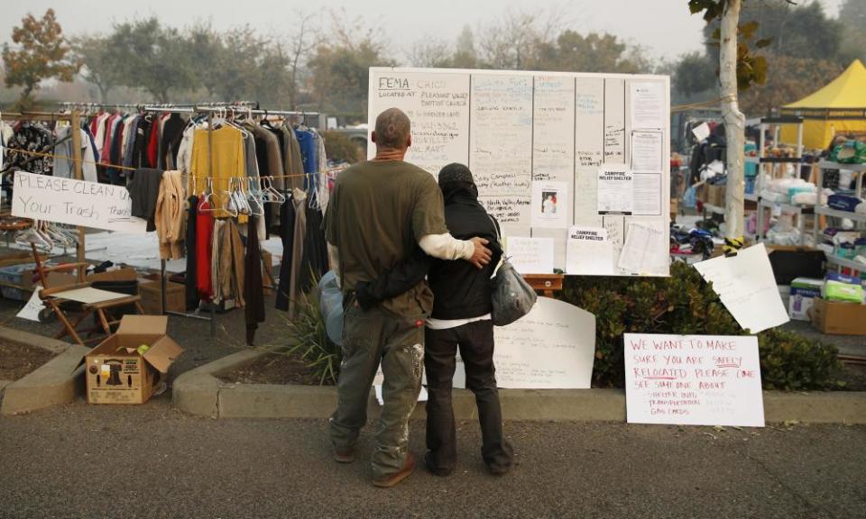 Tera Hickerson, right, and Columbus Holt embrace as they look at a board with information for services at a makeshift encampment outside a Walmart for people displaced by the Camp fire.