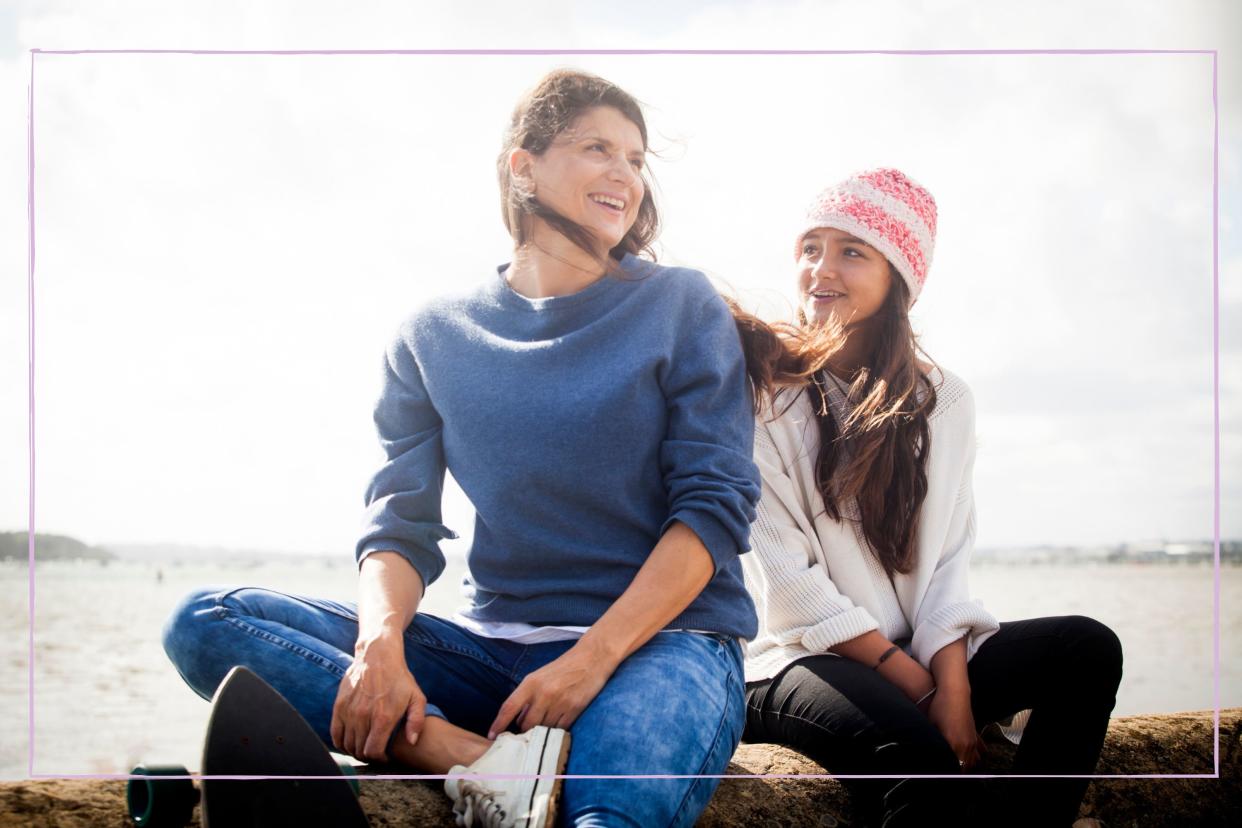  Mother sat with teenage daughter on a beach. 