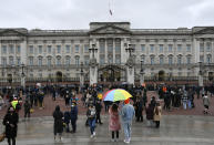 A couple under an umbrella gather with others outside the gates at Buckingham Palace in London, a day after the death of Britain's Prince Philip, Saturday, April 10, 2021. Britain's Prince Philip, the irascible and tough-minded husband of Queen Elizabeth II who spent more than seven decades supporting his wife in a role that mostly defined his life, died on Friday. (AP Photo/Alberto Pezzali)