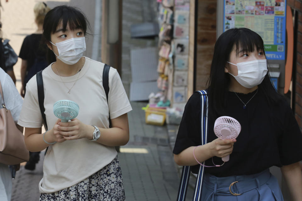 People wearing face masks to help protect against the spread of the coronavirus hold portable fans to cool themselves in the heat in Tokyo, Wednesday, Aug, 5, 2020. (AP Photo/Koji Sasahara)