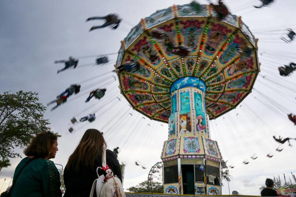Fairgoers watch riders spin on the Wave Swings during the opening day of the Miami-Dade County Youth Fair at the Miami-Dade Fair & Expo Center in Miami, Florida, on Thursday, March 17, 2022.