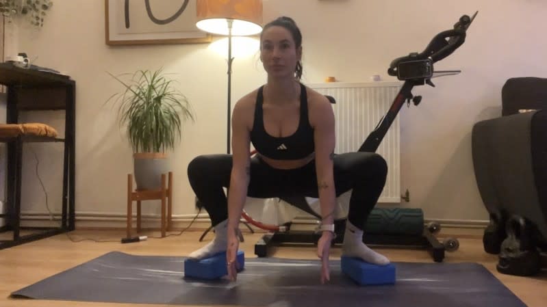 Sam performing a sumo squat with hands down and feet raised on blocks