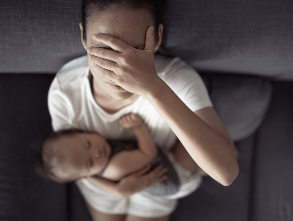 Woman sitting with a sleeping baby on her lap, holding her head in distress