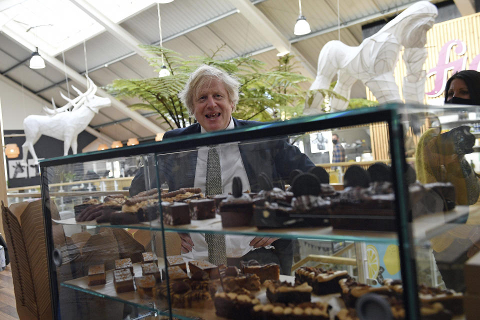 Britain's Prime Minister Boris Johnson looks at a display of cakes and desserts during a visit to Lemon Street Market in Truro, England, Wednesday, April 7, 2021 to see how they are preparing to reopen ahead of Step 2 of the roadmap on Monday. Johnson has confirmed that businesses from barbers to bookstores will be allowed to reopen next week and that Britain's slow but steady march out of a three-month lockdown remains on track. (Justin Tallis/Pool Photo via AP)