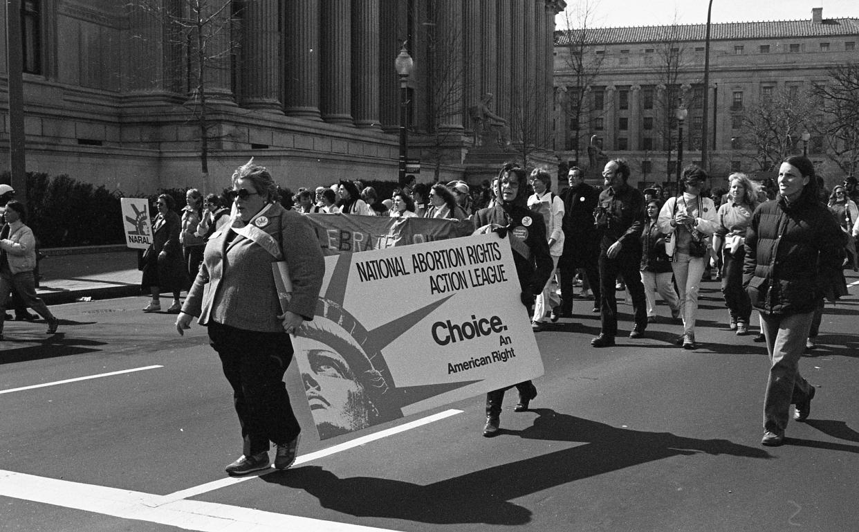 Demonstrators passing government buildings with columns carry a placard saying: National Abortion Rights Action League: Choice, An American Right.
