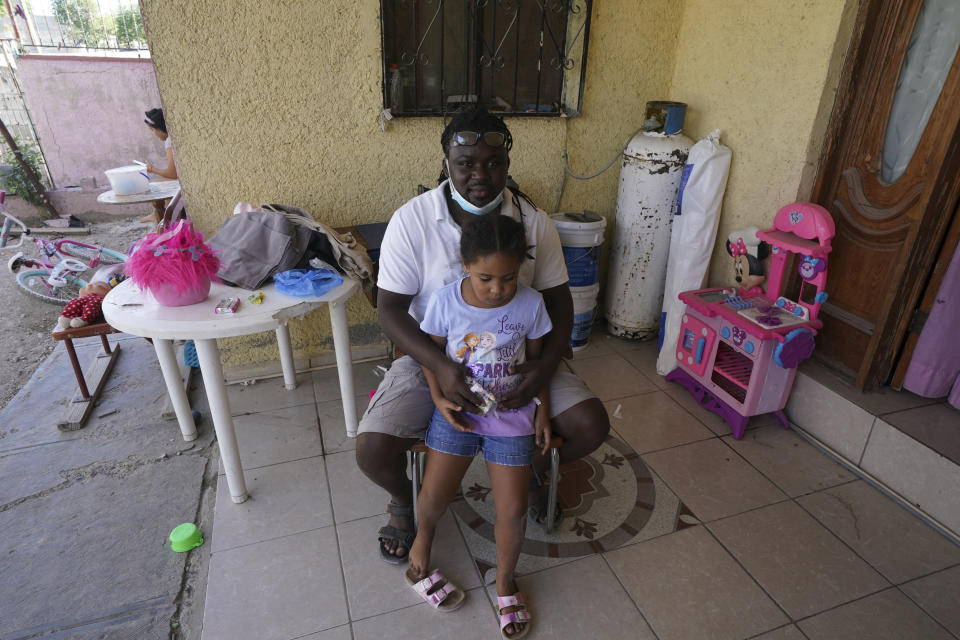 Mensah Montant and his daughter Rachel sit on their porch in Ciudad Acuna, Friday, Sept. 24, 2021. Montant, from the African nation of Togo, and his wife, are among the Acuna residents who are responding to the needs of Haitian migrants. (AP Photo/Fernando Llano)