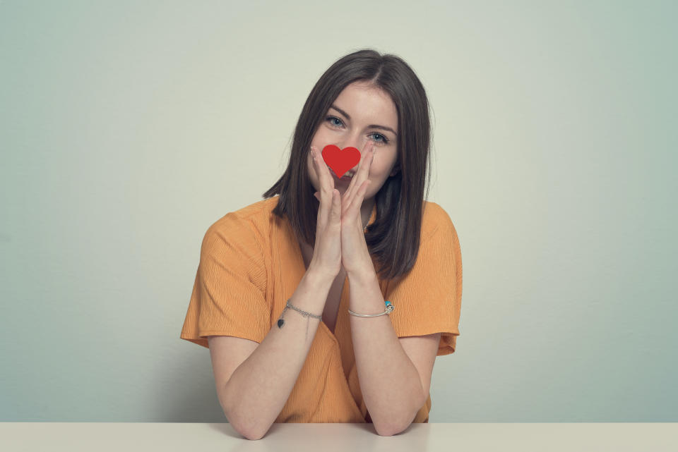 Smiling young woman holding a heart shaped in front of her face