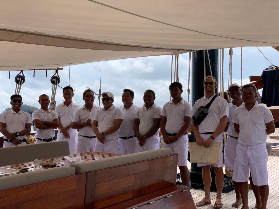 A group of crew members on board a yacht standing in line in white uniforms.