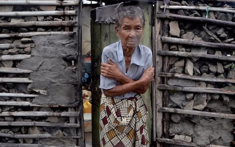 A shivering displaced woman is portrayed in the doorframe of a house in Beira 