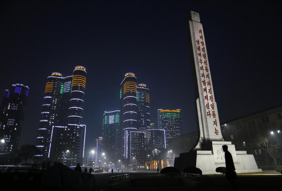 In this Tuesday Feb. 25, 2014 photo, a North Korean man walks past a tower with words " Our great comrades Kim Il Sung and Kim Jung Il will always be with us " near a residential complex which is lit at night in Pyongyang, North Korea. (AP Photo/Vincent Yu)