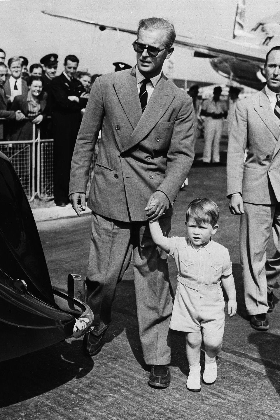 <p>Walking hand-in-hand with his father, Prince Phillip, at the London airport upon the family's return from Malta.</p>