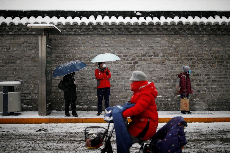 People wearing masks wait amid snow at a bus stop as the country is hit by an outbreak of the novel coronavirus, in Beijing