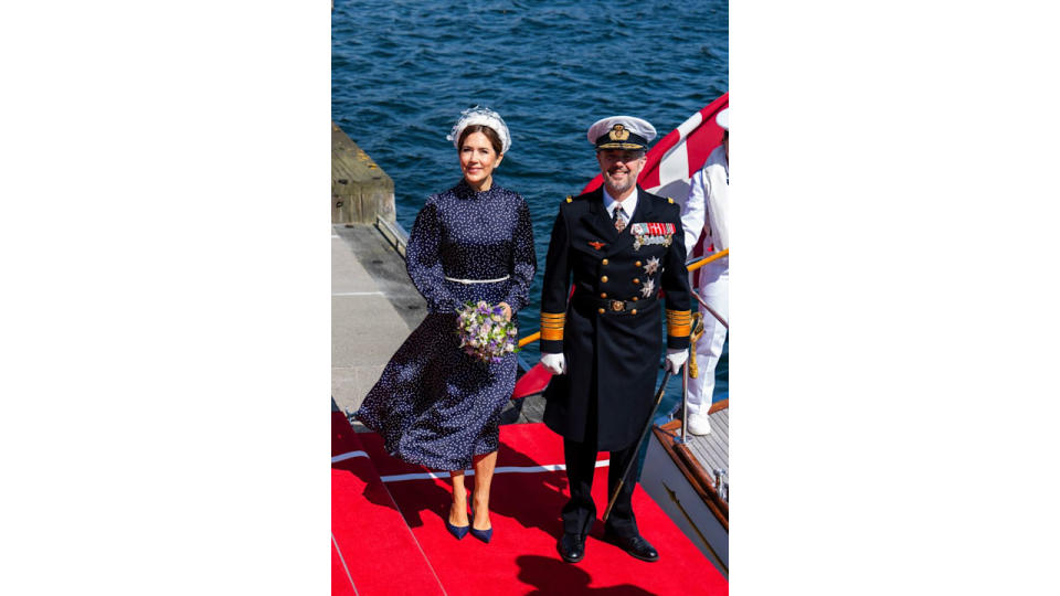 Queen Mary holding a bunch of flowers standing with King Frederik who wears a naval uniform