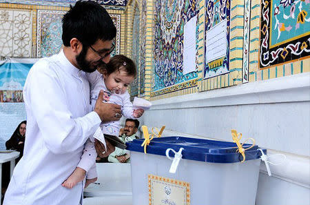 An Iranian man holds a girl as he casts his vote during a second round of parliamentary elections, in Shiraz, Iran April 29, 2016. Farsnews.com/Handout via REUTERS