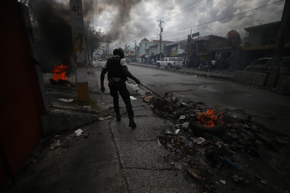 A policeman uses a rake to drag burning tires out of the road as police break up a barricade in Port-au-Prince, Haiti, Wednesday, Oct. 2, 2019. A group of men was protesting at the intersection after commissioning a mural of opposition organizer Jose Mano Victorieux, known as "Badou," who they said was executed Saturday night by unknown assailants.(AP Photo/Rebecca Blackwell)