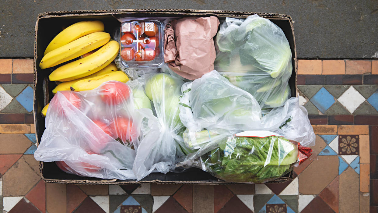 Overhead view of a box of fruit and vegetables is hand delivered and left on the doorstep.