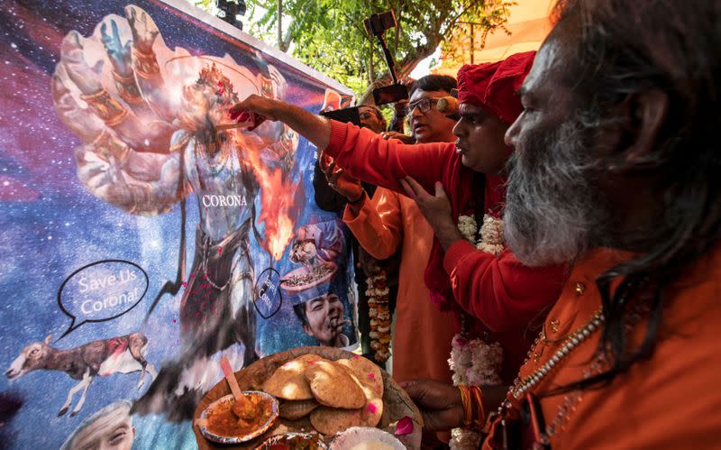 Members of All India Hindu Mahasabha offer cow urine to a caricature of coronavirus as they attend a gaumutra (cow urine) party in New Delhi