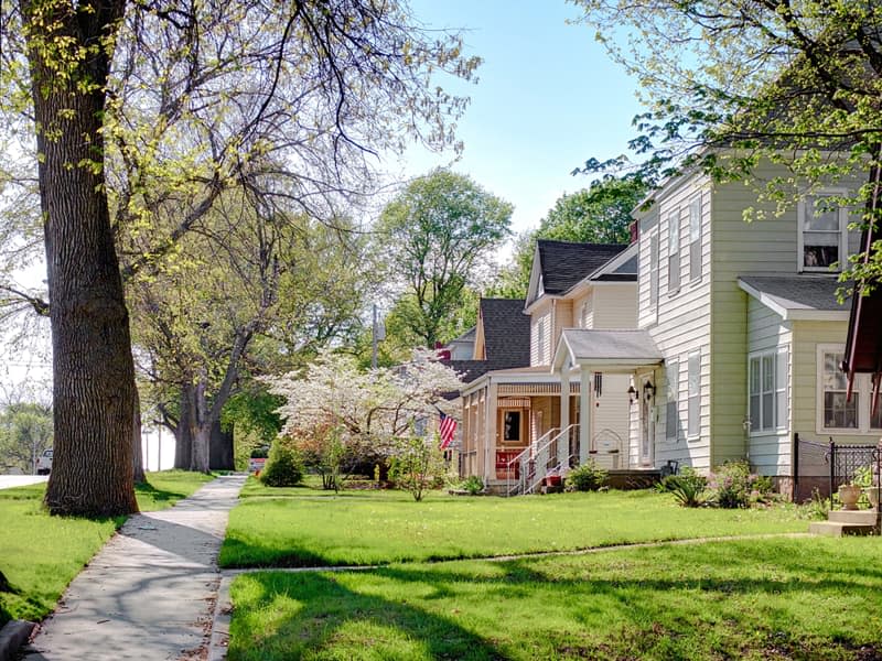 View on country street with private houses among blossom trees and lawns. American traditional country real estate architecture