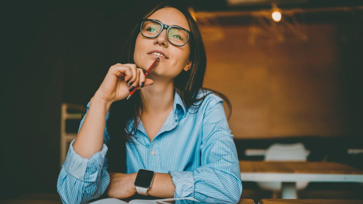 Dreamy woman podring while working on journalistic publication sitting with notebook in cafe,thoughtful female student in eyewear doing homework task solving problems and analyzing information.